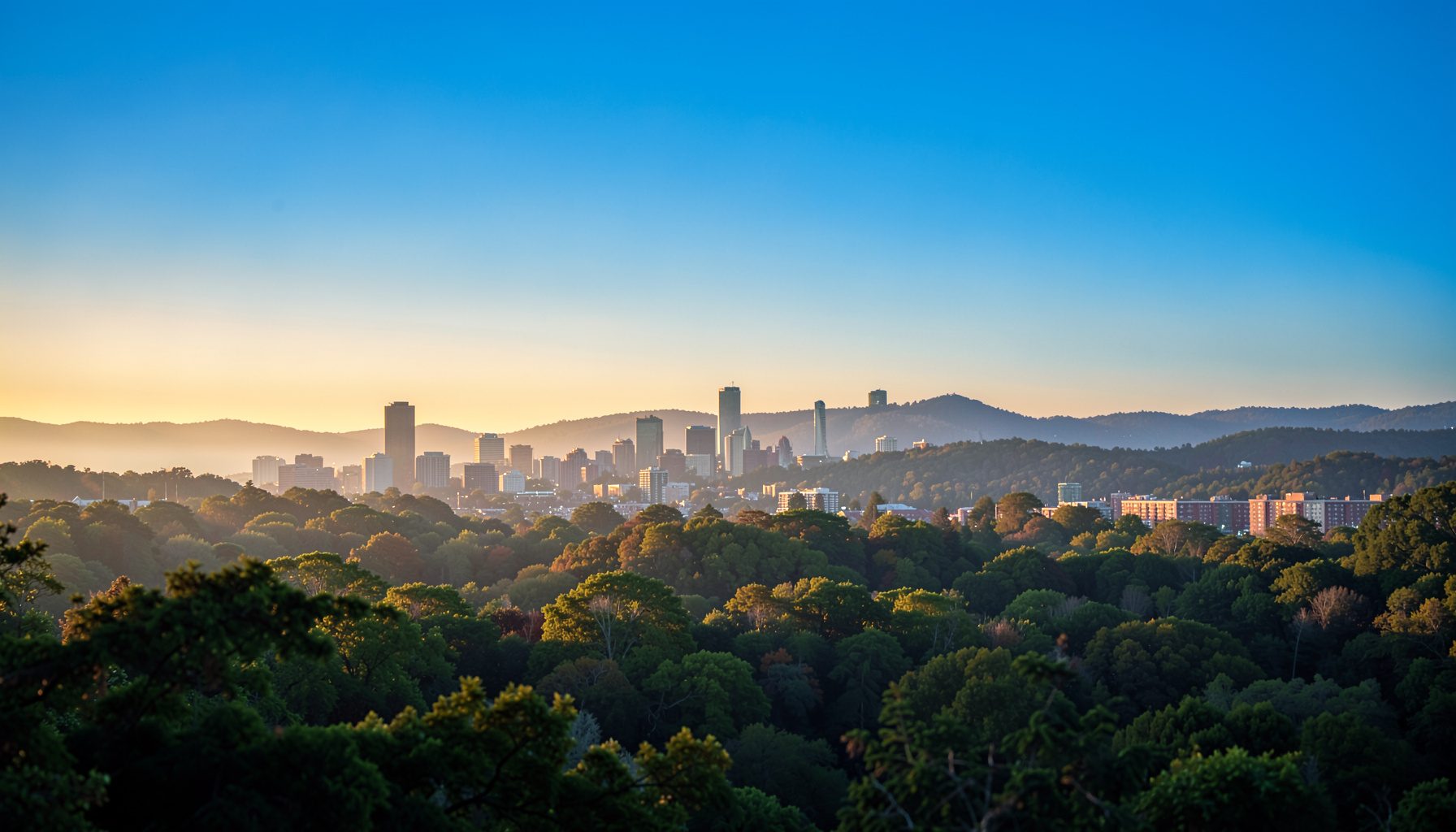 Wide landscape view of the Research Triangle skyline at golden hour, soft haze over distant tree-covered hills, warm amber and muted blue tones