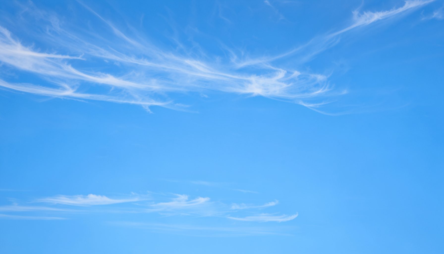 Soft blue sky with thin white cirrus clouds stretching across a wide horizon, calm and open atmosphere